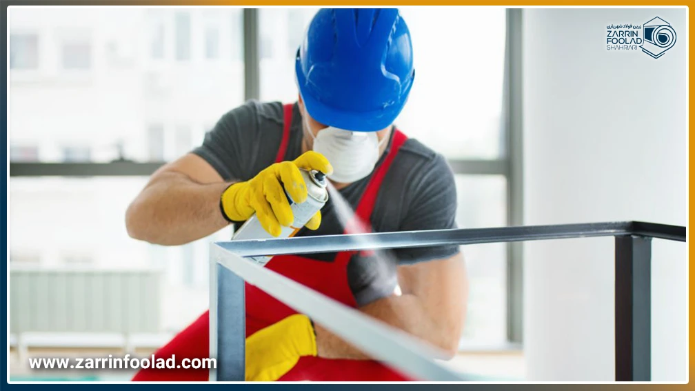 یک مرد با لباس و کلاه ایمنی در حال رنگآمیزی چهارچوب میز ساخته شده با پرفیل